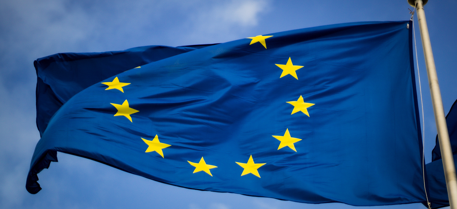 EU-lippu liehuu lipputangossa sinistä taivasta vasten.