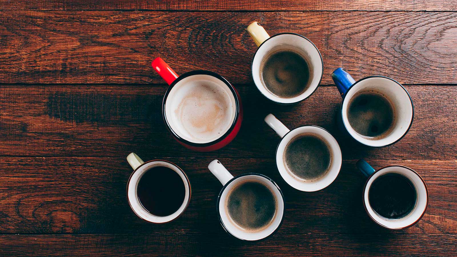 Pöydällä on erikokoisia ja erivärisiä kahvikuppeja, joissa on erilaista kahvia.