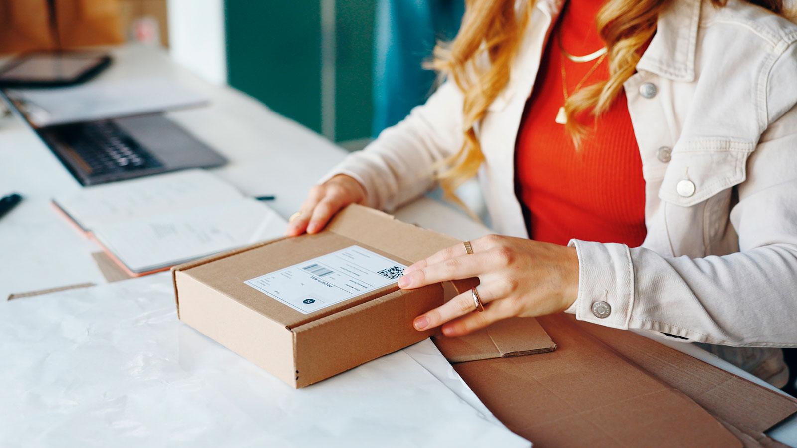 Nainen avaa postipakettia työpöydällään. Kuva: Mostphotos.