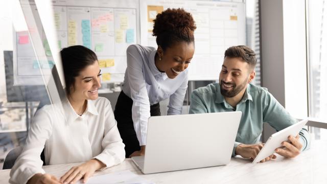 Joukko kollegoita työskentelee yhdessä pöydän ääressä läppärillä.