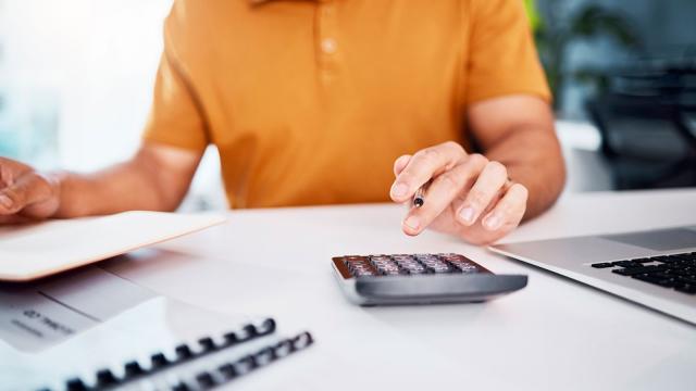 Henkilö istuu työpöytänsä ääressä ja tekee laskelmia. Kuva: Mostphotos.