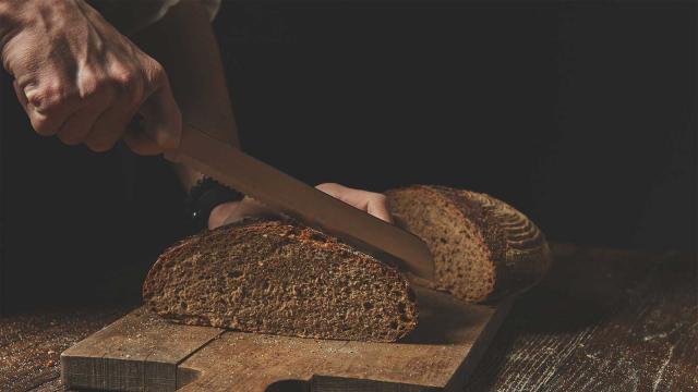 Mies leikkaa leikkuulaudalla olevaa tuoretta ruisleipää. Kuva: Pixhill.