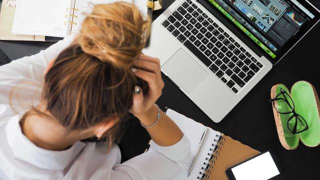 Stressaantunut nuori nainen nojaa päätään käsiinsä työpöytänsä ääressä. Kuva: Pexels / Energepics.com.