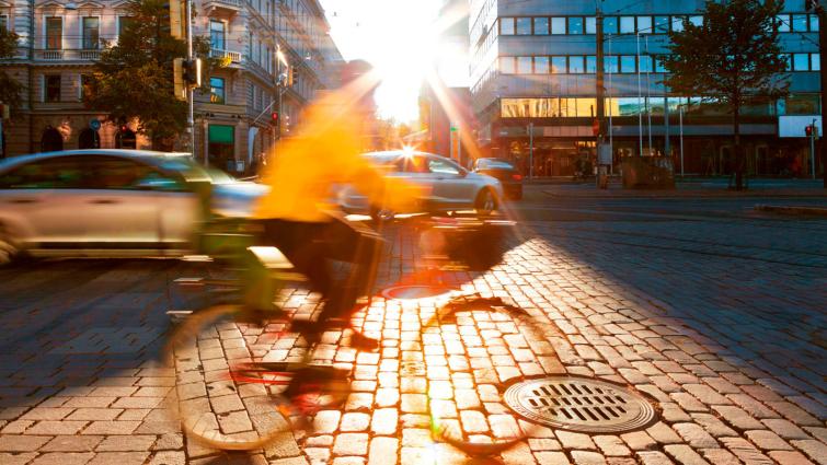 Keltaiseen takkiin pukeutunut ihminen pyöräilee kaupungin kaudulla. Kuva: iStock.