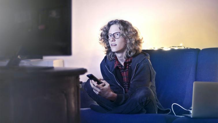 Nuori mies katsoo televisiouutisia ja käyttää tietokonetta samaan aikaan.