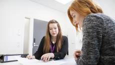 Kaksi naista katsovat pöydän ääressä papereita ja keskustelevat niiden sisällöstä.