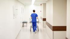 Kuvassa hoitaja työntää sairaalasänkyä sairaalan käytävällä. Hänellä on selkä kameraan päin.
