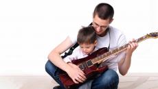 Isä ja poika harjoittelevat kitaran soittoa.