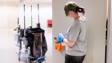 Henkilö puhdistaa oven kahvaa, taustalla siivouskärry. Kuva: Eeva Anundi.