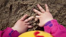 Lapsi hiekkalaatikolla. Kädet hiekassa. 